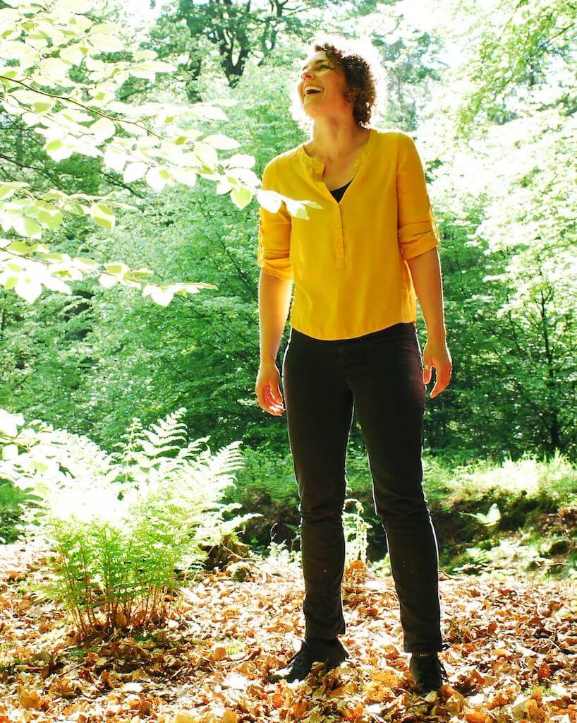 Een foto van een vrouw in het bos, lachend en omhoog kijkend